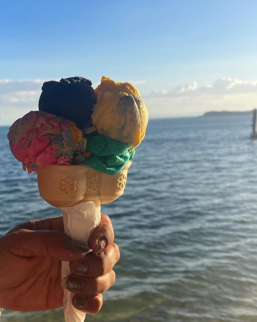 Four scoops of ice cream in a waffle cone, held up against the passage with the far shore on the horizon behind.